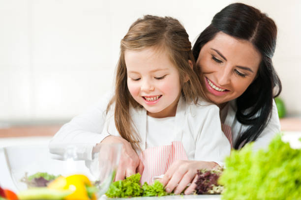A Mum and a daughter smiles while chopping fresh vegetables, preparing a healthy meal and fostering a positive relationship with food.