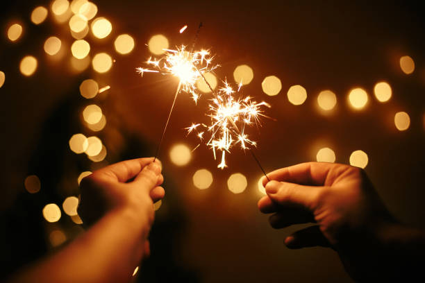 A close-up of hands holding sparklers, the vibrant sparks creating a trail of light against a dark background