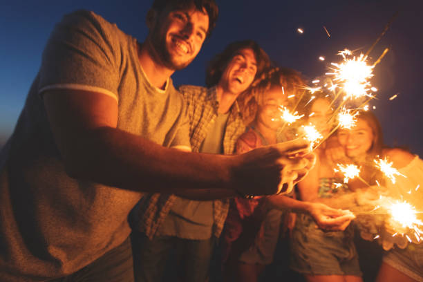 A family gathered around a bonfire on a summer night, holding sparklers that cast a warm glow on their faces
